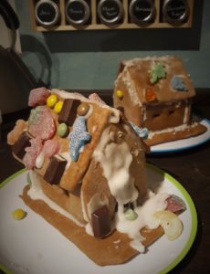 Zwei reichlich mit Süßigkeiten verzierte Lebkuchenhäuser stehen vor einer türkisen Wand.